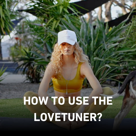Woman sitting cross-legged outdoors, wearing a white cap and yellow outfit, using a Lovetuner necklace while meditating. Text overlay reads: 'How to use the Lovetuner?