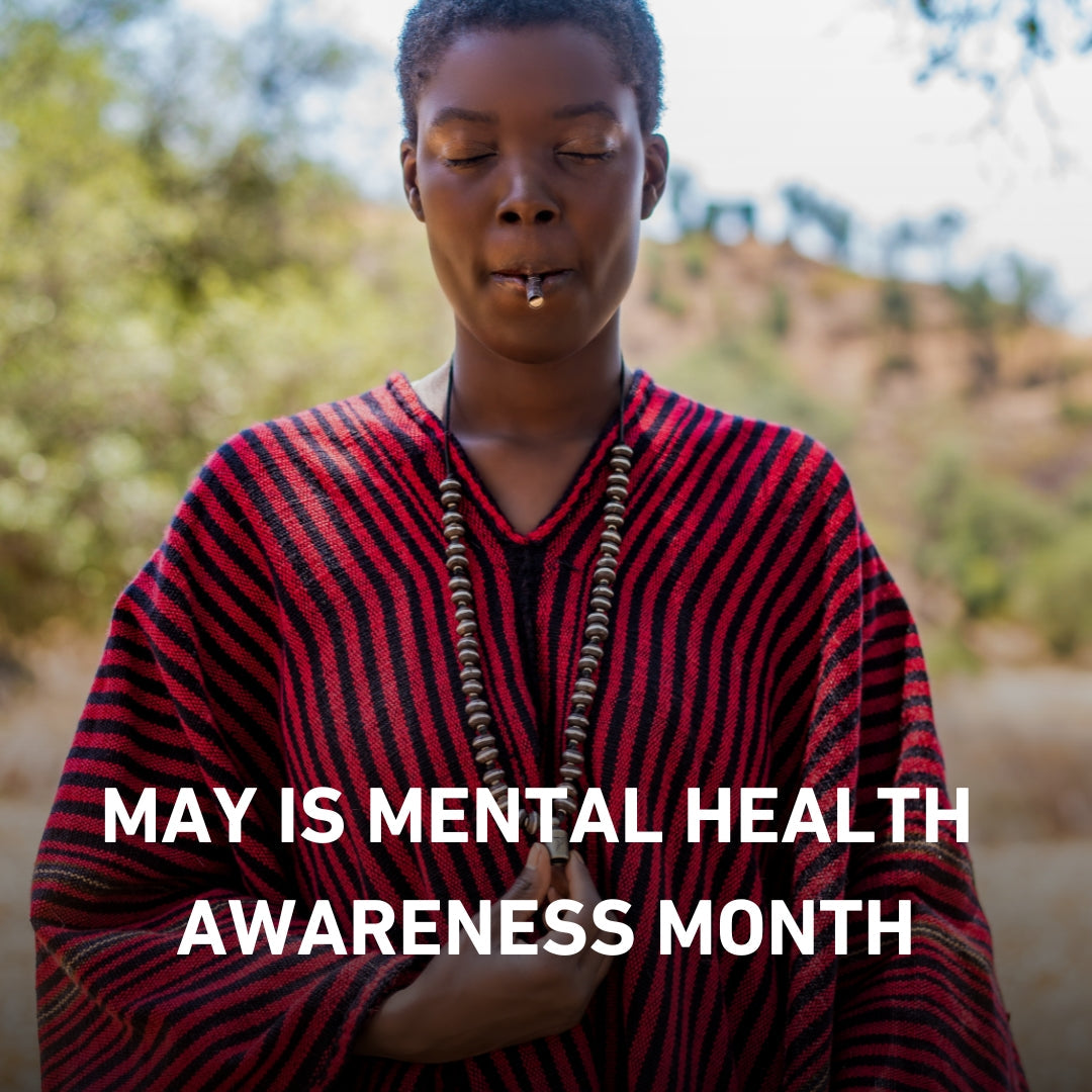 Person standing outdoors with eyes closed, wearing a red and black striped poncho and a beaded necklace, promoting Mental Health Awareness Month.