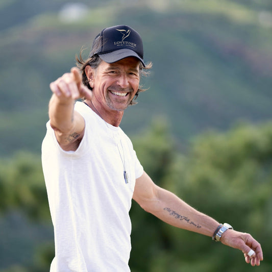 Sigmar Berg wearing a Lovetuner cap and white shirt, pointing towards the camera outdoors, with mountains in the background
