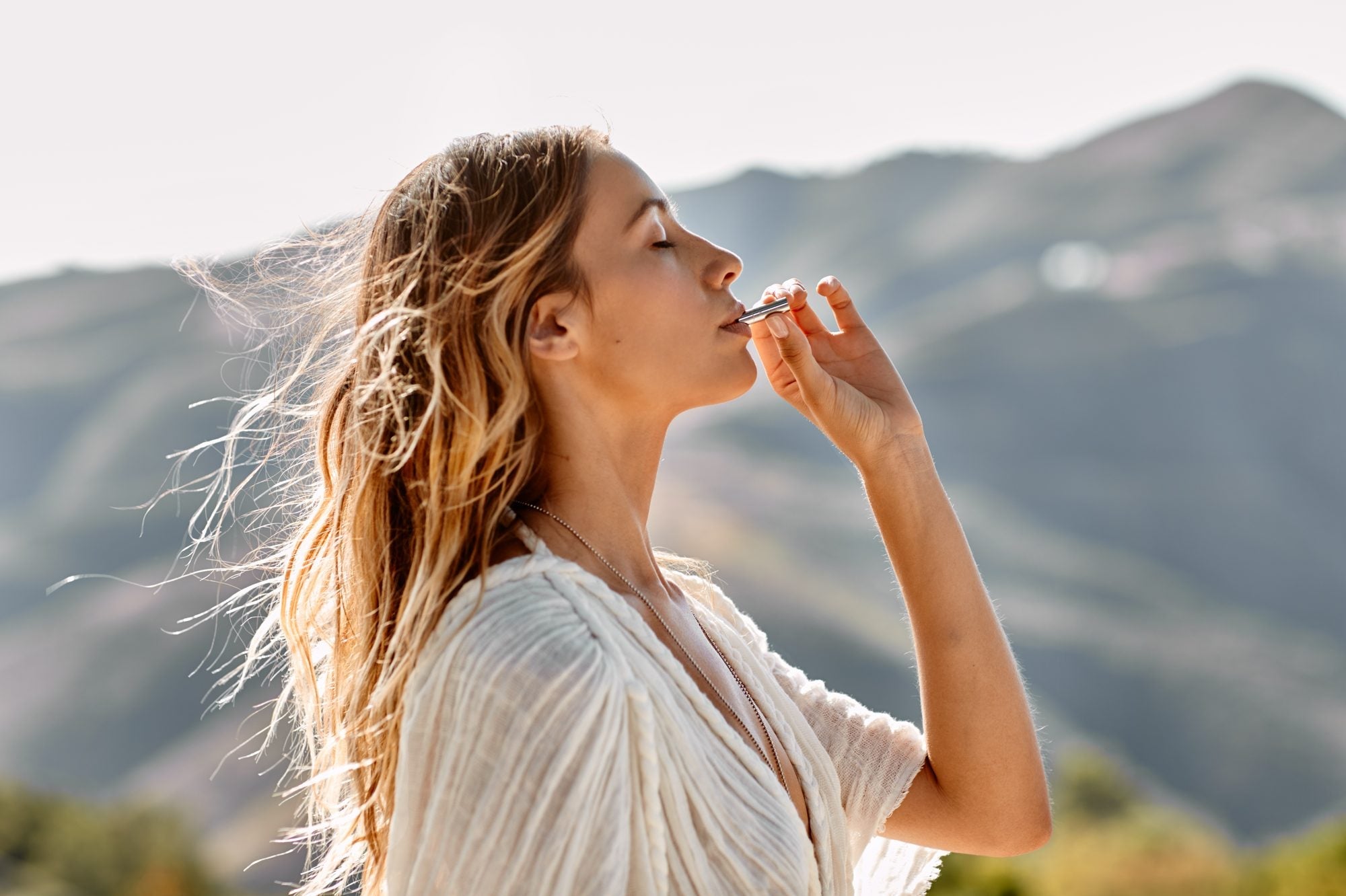 Woman with eyes closed exhaling through a Lovetuner to tune into 528 Hz in the mountain sunlight