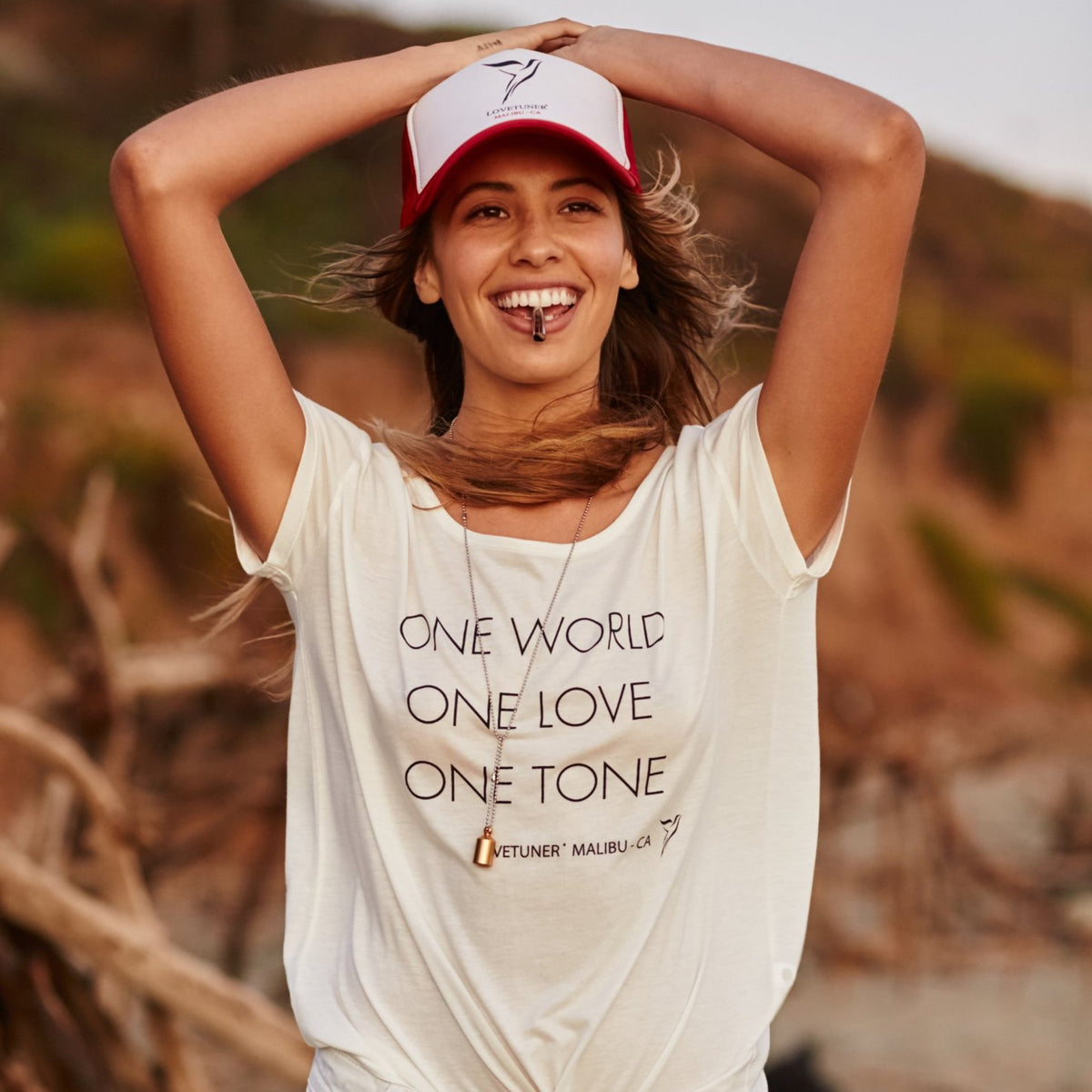 Woman on the beach wearing a Lovetuner 528Hz breathing necklace and One World One Love One Tone t-shirt