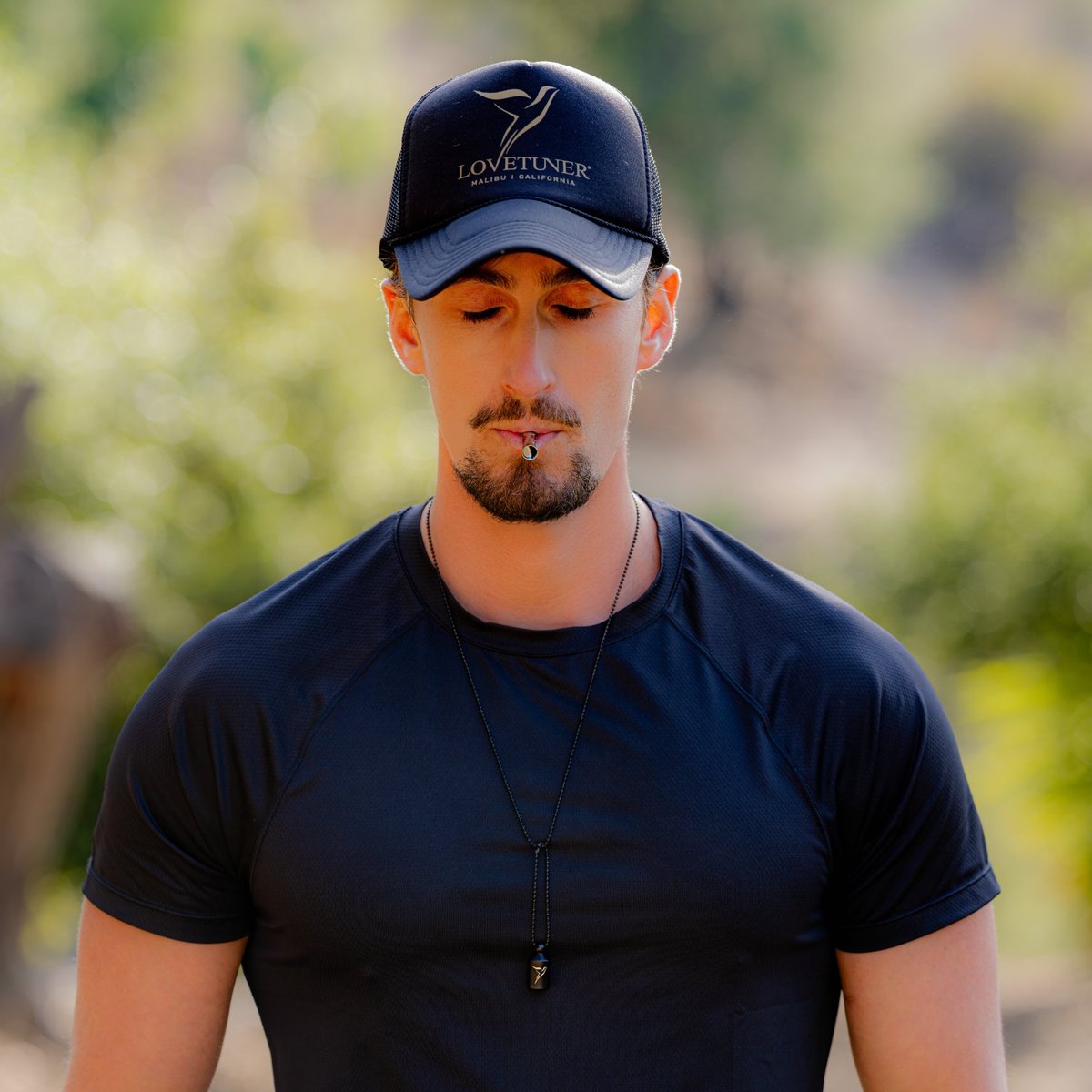 Man in a Lovetuner cap breathing through the 528 Hz breathing necklace with eyes closed to focus