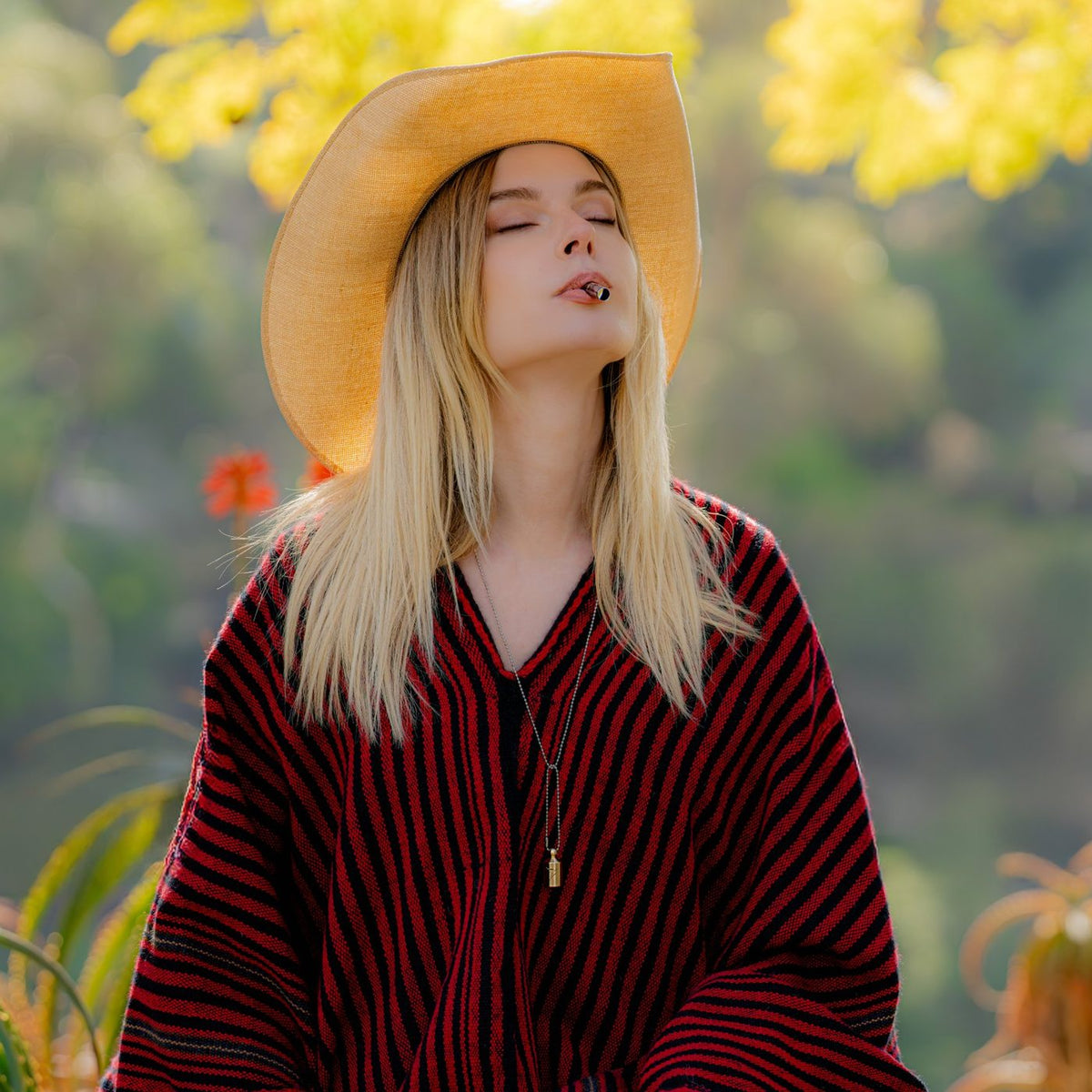 Woman in a straw hat breathing through a gold Lovetuner 528 Hz necklace with her eyes closed, outdoors among autumn leaves