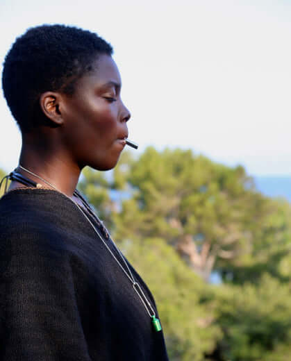 A women blowing a Lovetuner whistle with against blurry backdrop above trees with a calm expression