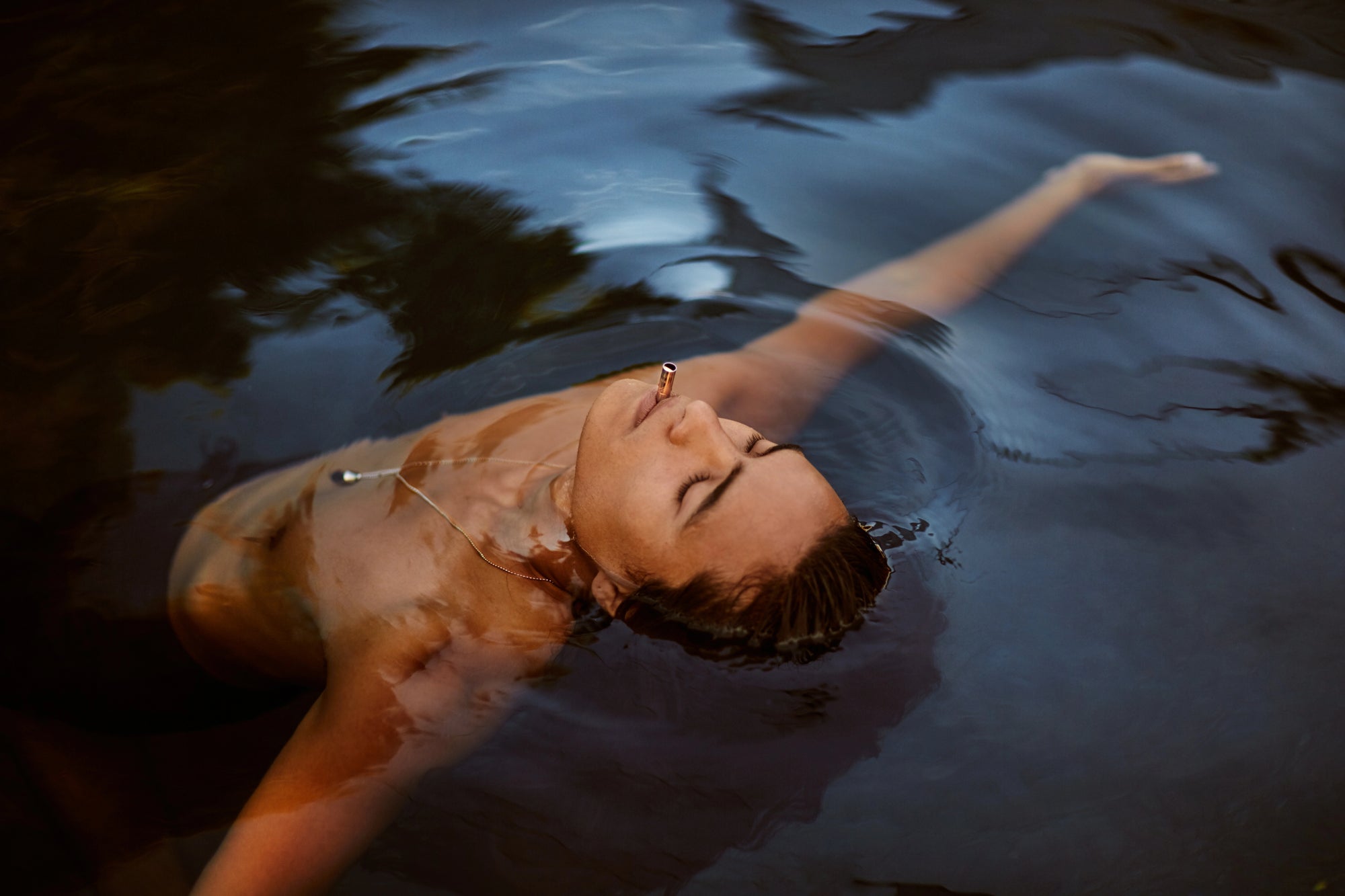 Person floating in water with a serene expression and a Lovetuner in their mouth