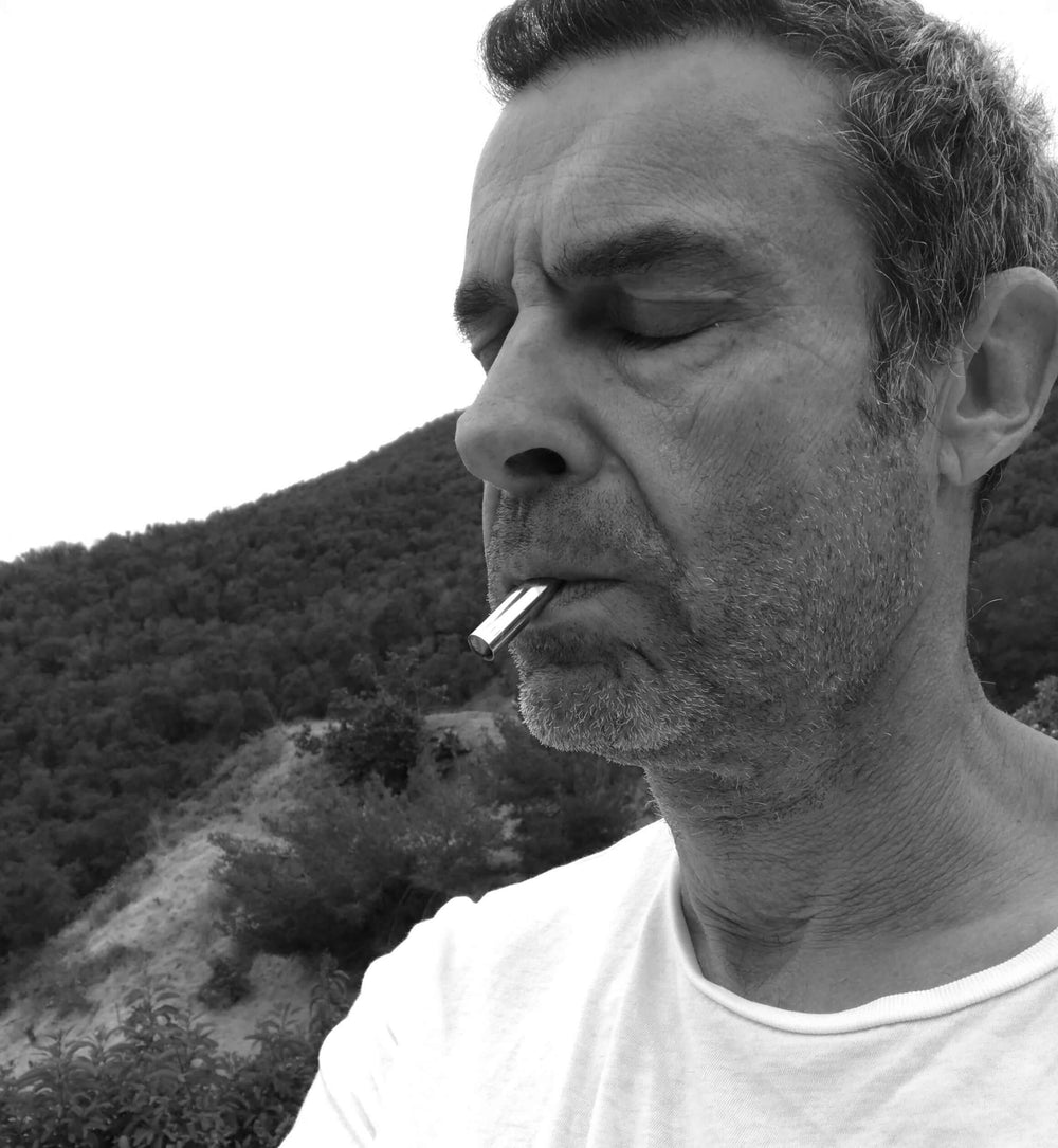 A black and white photo of a man in a white t-shirt with his eyes closed using the Lovetuner with the mountain behind him