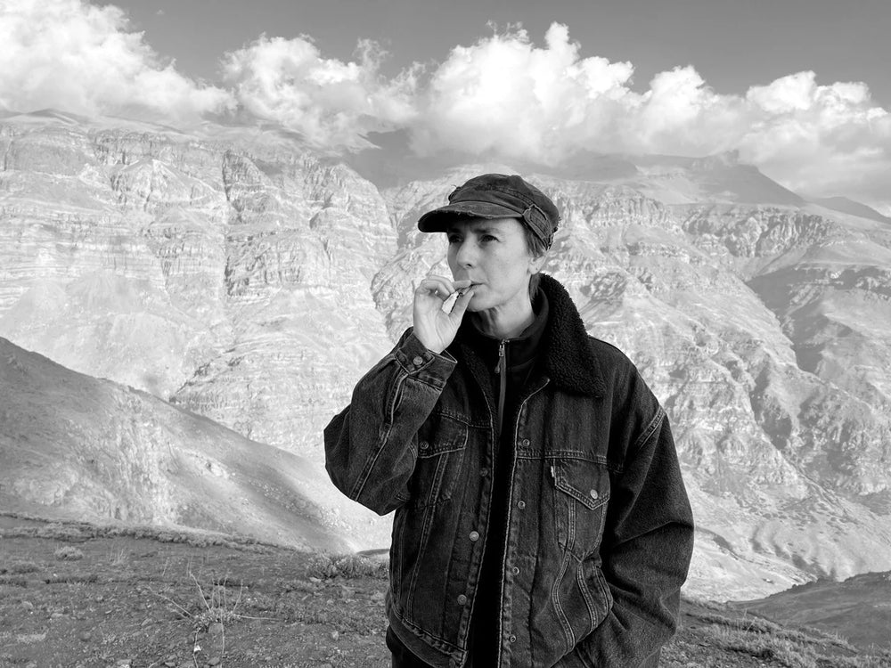 A black and white photo of a woman in a cap and denim jacket using the Lovetuner against a backdrop of rolling mountains