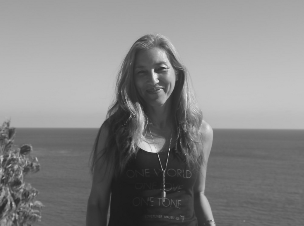 A photo of a woman near the sea wearing a Lovetuner and a One World. One Love. One Tone. tank top