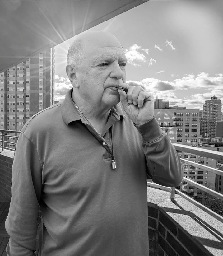 A black and white photo of a bald older man using the Lovetuner atop a building with the sun creating a halow around his head