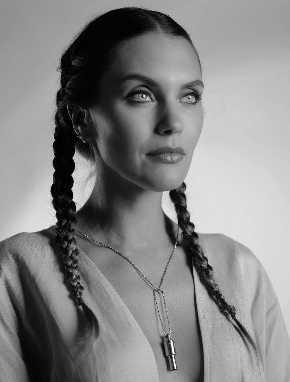 Woman with braided hair wearing a necklace against a plain background