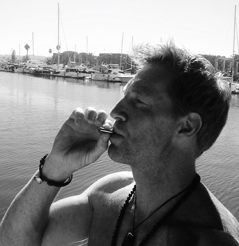 A shirtless man using a Lovetuner near a body of water with boats in the background behind him