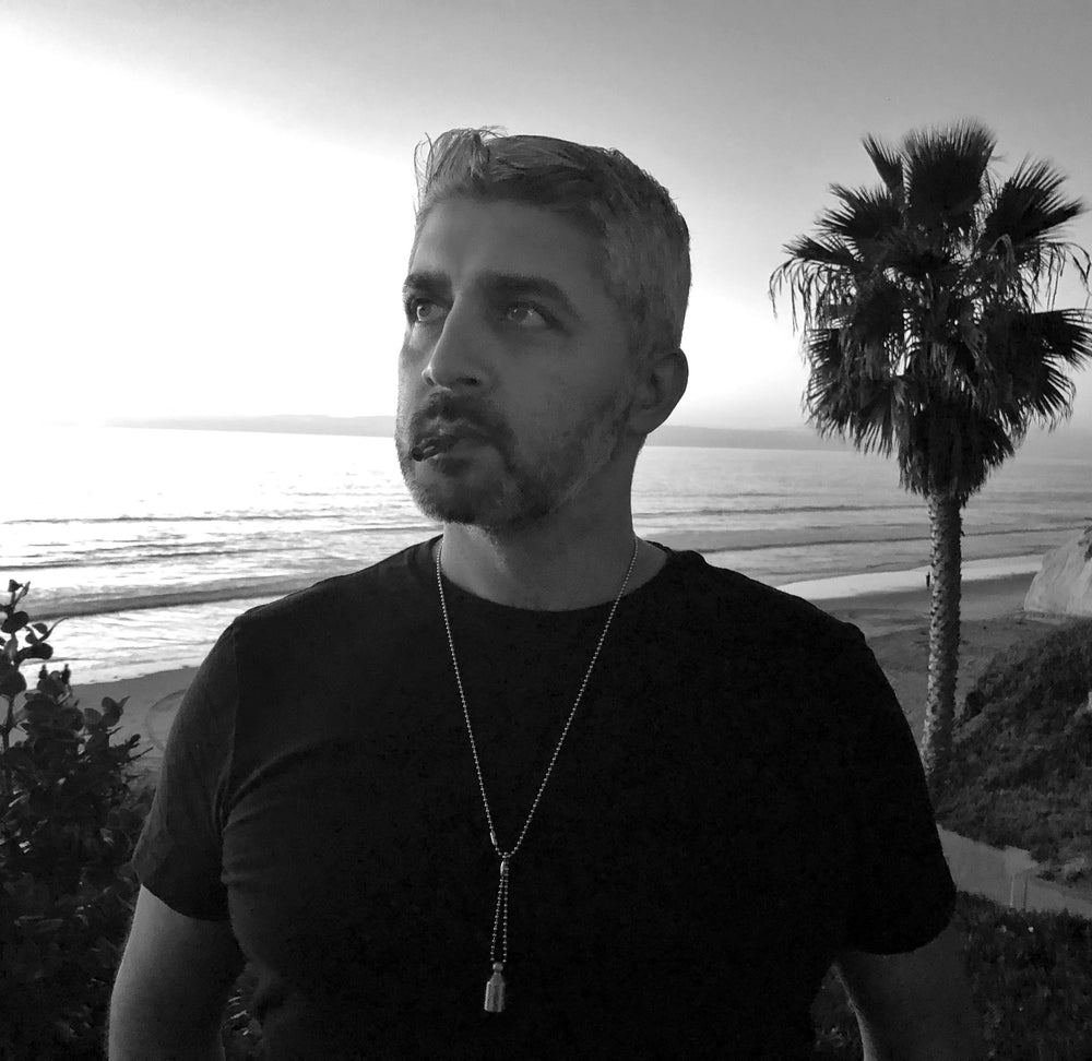 A black and white photo of an Indian man using the Lovetuner with a palm tree and the beach behind him