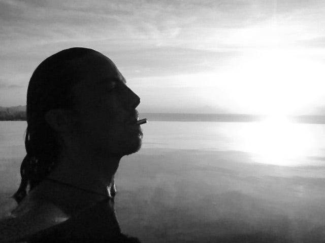 A black and white photo of a man in a body of water up to his shoulders using the Lovetuner with the sun setting behind him.