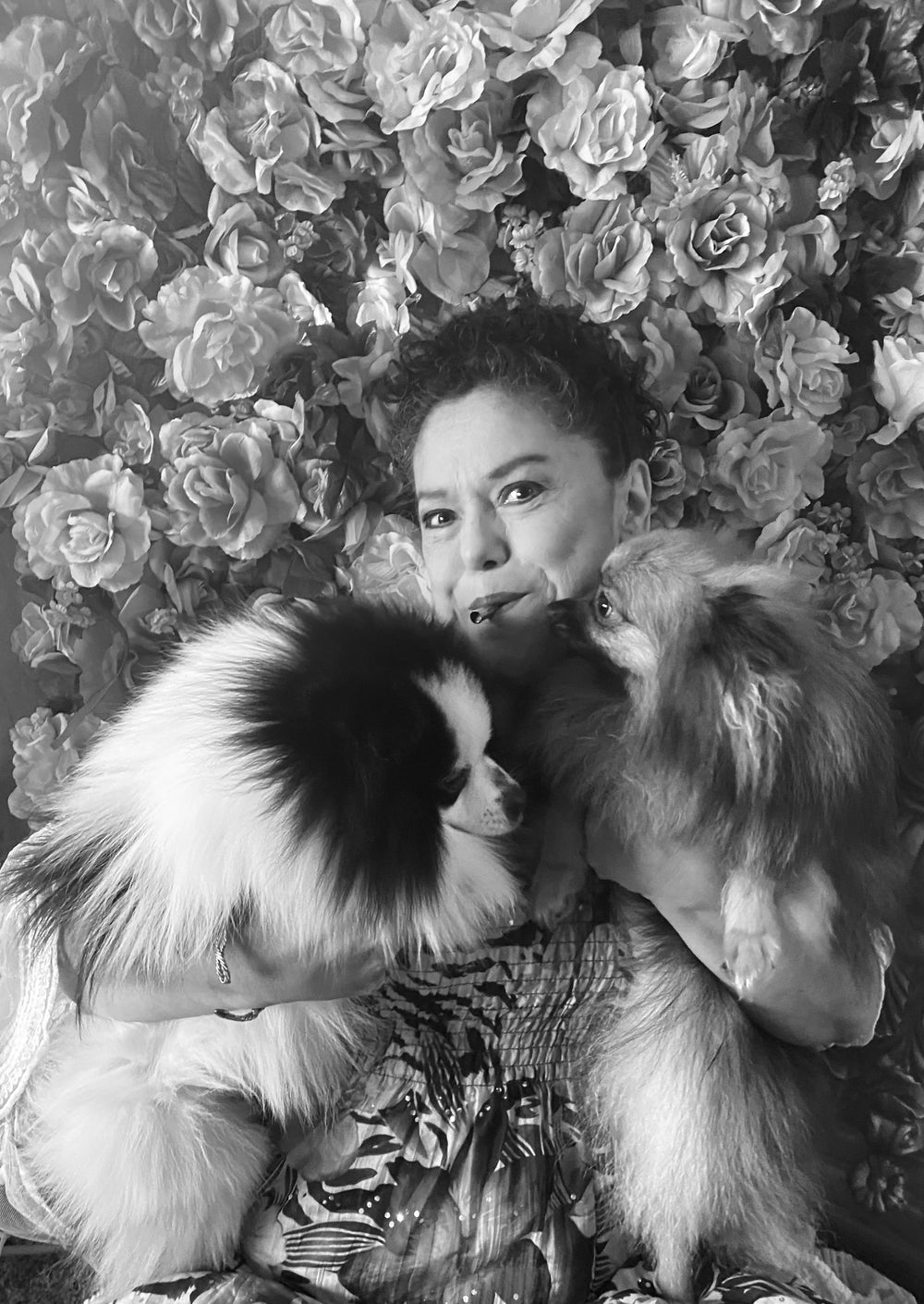 A black and white photo of a woman holding two dogs in her hands and using the Lovetuner against a backdrop of flowers on a wall